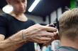 © Maria Sbytova - Hairdresser is cutting hair of handsome bearded mature man in salon. Stylist making hairstyle with electric shaver for person in barbershop. Services of a professional stylist. Fashion haircut