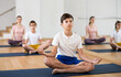 Young boy practicing lotus pose during family yoga training in fitness studio.