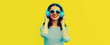 Portrait of happy smiling young woman with headphones listening to music on yellow background, blank copy space for advertising text