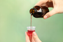 Woman Pouring Cough Syrup Into Measuring Cup On Light Green Background, Closeup