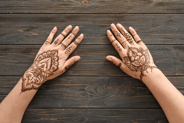 Wall Mural - Female hands with beautiful henna tattoo on wooden background