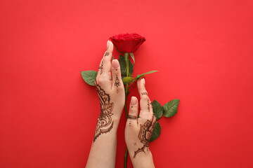Wall Mural - Female hands with beautiful henna tattoo and rose flower on color background, closeup