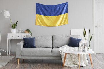 Interior of light living room with hanging Ukrainian flag, sofa and houseplants