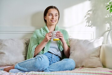 young female resting with cup of hot tea, sitting on couch at home