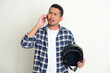 Adult Asian man holding motorcycle helmet and showing confused expression when answering a phone call