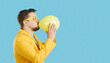 Side view of young Caucasian man isolated on blue studio background blow air balloon. Narrow wide shot of guy with airbaloon. Fun and entertainment. Copy space, empty advertising placement.