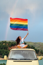 Smiling Young Woman Holding Rainbow Flag Sitting On Van