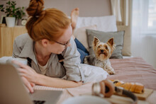 Woman Lying With Laptop Looking At Pet Dog On Bed At Home
