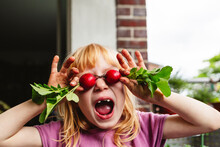 Girl With Mouth Open Covering Eyes With Radish On Balcony