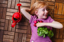 Happy Girl With Radish Lying By Watering Can On Balcony Floor