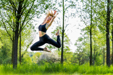 Young Woman Jumping Over Meadow At Park