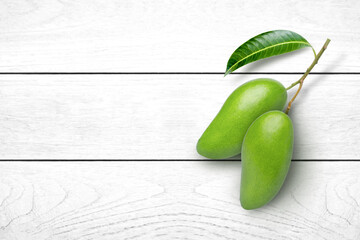Wall Mural - Green mango fruit with green leaf isolated on white wooden table background. Top view. Flat lay.