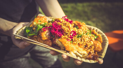 Wall Mural - Street food - Hand holding portion of spicy chicken wings with red cabbage and herbs