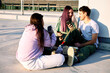 © chika_milan - Happy teenage friends are sitting in urban exterior and using their phones for hanging on social media.