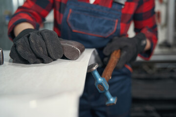 Female auto mechanic working with hammer in car repair garage