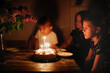 Cute kid girl blows out the candles on a birthday cake with her sisters, dark style. Cake and candle 9 years birthday celebration