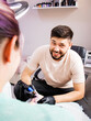 © Olga - Work as a tattoo artist in a tattoo parlor. a tattoo artist in black gloves is working on a tattoo on the leg of a young woman and looking at the client and smiling