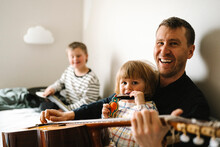 Portrait Of Happy Father With Guitar And Daughter Sitting In Bedroom