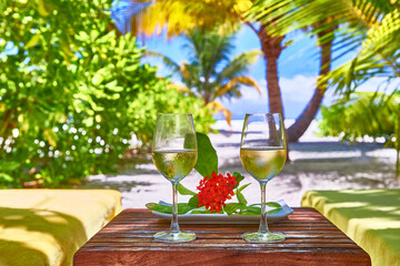 White wine in glasses near deck chair. Maldives beach resort. Amazing view, blue turquoise lagoon water, palm trees and white sandy beach. Luxury travel vacation destination