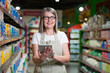 © Liubomir - Portrait of senior woman in glasses consultant, employee in grocery store, supermarket. Stands with a tablet, accepts the goods, checks. In work clothes