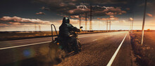 Stylish Brutal Biker Riding Motorbike In Speed Highway In Summer Evening Time. Vintage Cinematic Background And Dramatic Cloudy Sky. Concept Of Fashion, Style And Hobby