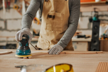 Wall Mural - Close up of young carpenter sanding wood while building handcrafted furniture in workshop, copy space