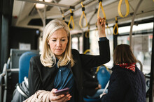 Businesswoman Holding Grab Handle While Using Smart Phone In Bus