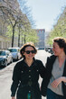 © Maskot - Cheerful lesbian couple walking on street in city during sunny day