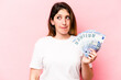 © Asier - Young caucasian woman holding banknotes isolated on pink background confused, feels doubtful and unsure.