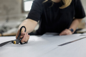 Close-up of dressmaker cutting piece of fabric with scissors in sewing workshop. Process of manufacturing a piece of clothing or upholstery for upholstered furniture made of fabric in studio workshop