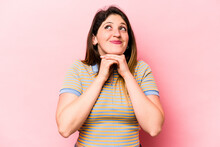 Young Caucasian Woman Isolated On Pink Background Keeps Hands Under Chin, Is Looking Happily Aside.