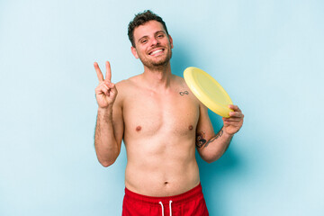 Young caucasian man playing with frisky isolated on blue background joyful and carefree showing a peace symbol with fingers.