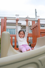 Wall Mural - Asian little girl child having fun while playing slider in the playground.