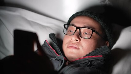 young chinese man lying and playing with mobile phone at night
