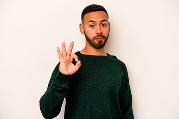 Wall Mural - Young hispanic man isolated on white background winks an eye and holds an okay gesture with hand.