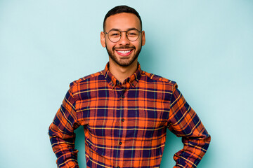 young hispanic man isolated on blue background confident keeping hands on hips.