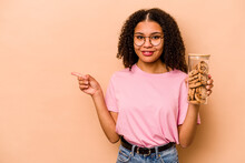 Young African American Woman Holding A Cookies Jar Isolated On Beige Background Smiling And Pointing Aside, Showing Something At Blank Space.