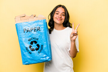 young hispanic woman recycling paper isolated on yellow background showing number two with fingers.