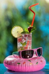 Wall Mural - summer beach concept, a drink with strawberries and lime, in a glass with a straw, next to an inflatable ring and glasses