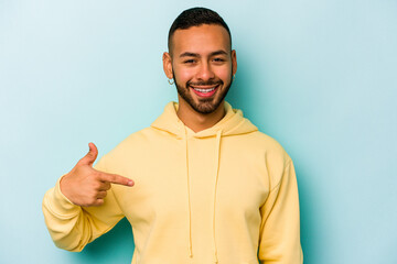 Wall Mural - Young hispanic man isolated on blue background person pointing by hand to a shirt copy space, proud and confident