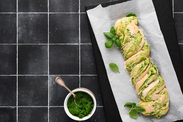 Braided wild garlic pesto brioche. Homemade raw or uncooked fresh pull apart bread with wild garlic pesto on wooden board on old black tile table background. Italian bread. Copy space. Top view.