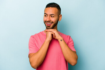 Wall Mural - Young hispanic man isolated on blue background praying for luck, amazed and opening mouth looking to front.