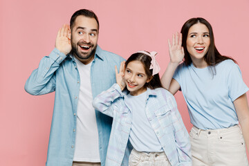 Wall Mural - Young happy curious parents mom dad with child kid daughter teen girl in blue clothes try to hear you overhear listening intently isolated on plain pastel light pink background. Family day concept.