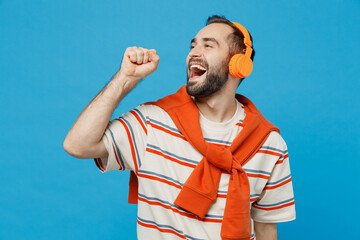 Wall Mural - Young smiling cheerful cool man 20s wearing orange striped t-shirt headphones listen to music sing song in microphone isolated on plain blue color background studio portrait. People lifestyle concept.