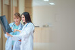 © Dearix - Young beautiful female doctor look at X-ray scan consult,diagnosis,discuss patient's log to senior doctor while walk in hospital hallway. Two different generation diversity multiracial medical concept