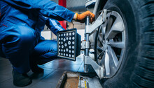 Auto Mechanic Installing Sensor During Suspension Adjustment And Automobile Wheel Alignment Work At Repair Service Station. Close Up