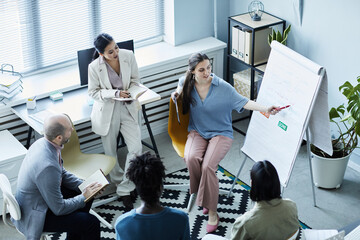 High angle view at young woman pointing at whiteboard during English lesson with diverse group of people sitting in circle in office