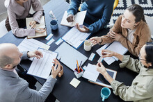 Top View At Diverse Group Of People At Meeting Table In Office Setting Communicating And Gesturing