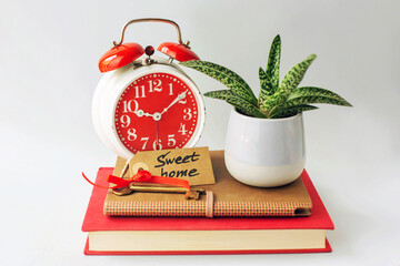 A red alarm clock, a flower and a key with the inscription - sweet house are on books on a gray background.
