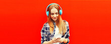 Portrait Of Happy Woman With Smartphone In Wireless Headphones Listening To Music On Red Background, Blank Copy Space For Advertising Text